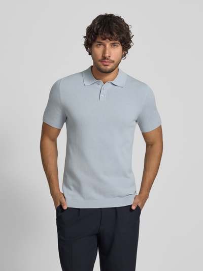 Männermodel trägt Slim Fit Poloshirt Modell 'Triton' von Drykorn, reine Baumwolle, hellblau, Strukturmuster, Polokragen, Ganzkörperansicht von vorne.