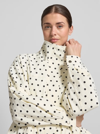 Frauenmodel trägt Jacke mit Stehkragen Modell 'CALLISA DOT' von Neo Noir im schwarzen Allover-Look auf cremefarbenem Stoff, Nahaufnahme Oberkörper. Rückenlänge 53 cm, Schulterbreite 53 cm, Brustweite 56 cm, Ärmellänge 54 cm, Regular-Fit, Damen Jacke.