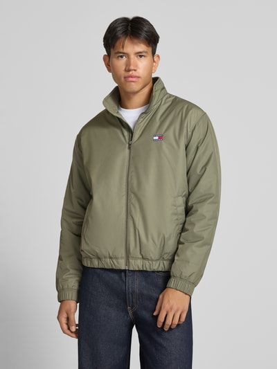 Männermodel trägt Regular Fit Blouson mit Label-Patch von Tommy Jeans, olivgrün, schlichte Struktur, Herren Bomberjacke, Ganzkörperansicht von vorne.