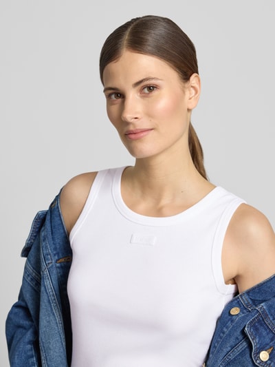 Modelka kobieca ma na sobie Tanktop in Ripp-Optik od JOOP!, bawełna z domieszką elastanu, krój slim fit, okrągły dekolt, biała fakturowana powierzchnia; zbliżenie na górną część ciała z przodu.