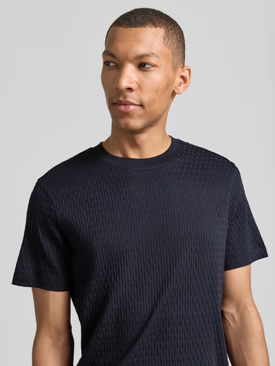 Männermodel trägt T-Shirt mit Strukturmuster Modell 'Raulos' von JOOP! Collection aus reiner Baumwolle, dunkles Blau, Nahaufnahme Oberkörper.