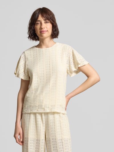 Kobiece model nosi bluzkę z krótkim rękawem z haftem angielskim model 'CASSANDRA' od Vero Moda, efekt: jednolity kolor, krój regular fit, okrągły dekolt, wykończenie materiału: haft angielski, jasny odcień, miękka faktura, przód, ujęcie: z przodu, górna połowa ciała