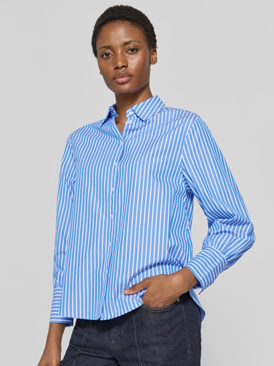 Frauenmodel trägt Regular Fit Hemdbluse aus reiner Baumwolle Modell 'VIC' von Brax mit blau-weißem Allover-Streifendesign, feine Webstruktur, einreihige Knopfleiste, Label-Applikation, Hemdkragen und langen Ärmeln, Nahaufnahme Oberkörper.