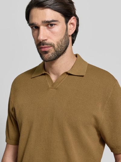 Męski model nosi Regular Fit Poloshirt mit gerippten Abschlüssen od MCNEAL z bawełny, kołnierzyk polo, krój regular fit, prążkowane wykończenia, długość tyłu 71 cm, długość rękawów 30 cm, kolor brązowy, faktura lekko prążkowana, nahaufnahme górnej części ciała.