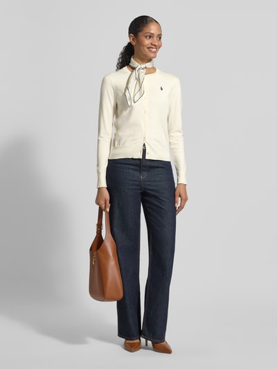 Frauenmodel trägt Regular Fit Strickjacke aus Baumwoll-Mix von Polo Ralph Lauren in Creme mit Logo-Stitching, Rundhalsausschnitt, Knopfleiste, elastische Abschlüsse, Jeans, Ganzkörperansicht von vorne. Kontext: Damen Strickjacke, Rückenlänge bei Größe S 52 cm, Ärmellänge bei Größe S 59 cm.