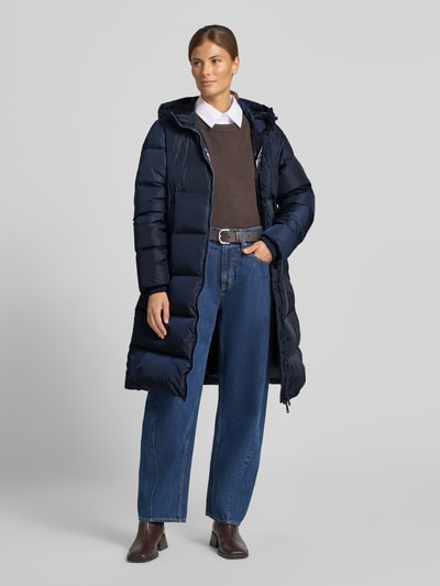 Frauenmodel trägt Steppmantel mit Zweiwege-Reißverschluss von Armani Exchange in Dunkelblau, wattiert, Kapuze, Reißverschlusstaschen, Storm Cuffs, gerade Passform, Kombination mit Jeans und Stiefeletten, Ganzkörperansicht von vorne.
