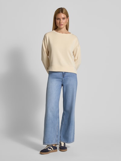 Frauenmodel trägt Relaxed Fit Sweatshirt mit Viskose-Anteil von comma in Beige, U-Boot-Ausschnitt, blaue Jeans, Ganzkörperansicht von vorne.