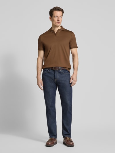 Männermodel trägt Regular Fit Poloshirt aus reiner Baumwolle von Tommy Hilfiger in Braun, unifarben, Logo-Detail, Ganzkörperansicht von vorne.