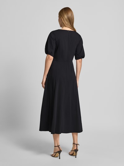 Vrouwenmodel draagt Midikleid met Raffungen van More & More in zwart met stolpplooi, katoenmix, getailleerd model, halflange mouwen, ruglengte 119 cm, borstwijdte 44 cm, mouwlengte 29 cm, Ganzkörperansicht Rückansicht.