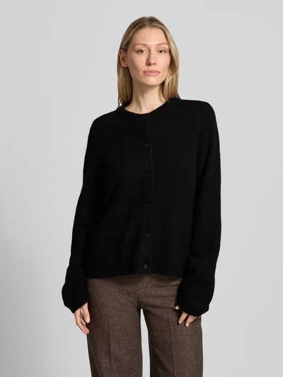 Frauenmodel trägt czarny kardigan rozpinany model 'LULU NEW' od Selected Femme, efekt: jednolity kolor, krój regular fit, listwa guzikowa, okrągły dekolt, długi rękaw, zakończenia rękawów i dołu: prążkowane, wykończenie materiału: dzianina, mieszanka wełny i alpaki. Ganzkörperansicht von vorne
