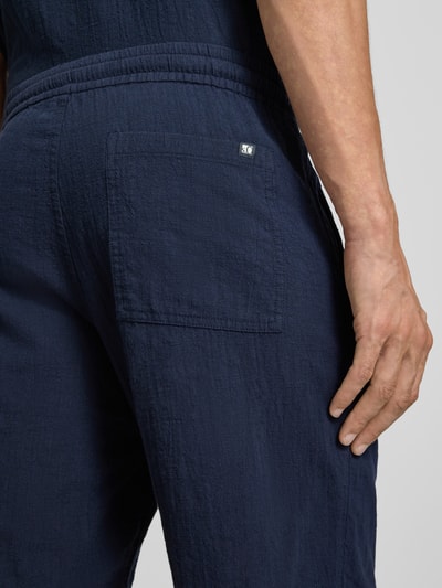 Männermodel trägt Relaxed Fit Stoffshorts aus einer Baumwolle von s.Oliver RED LABEL in Dunkelblau, strukturierte Oberfläche, Nahaufnahme Rückansicht.