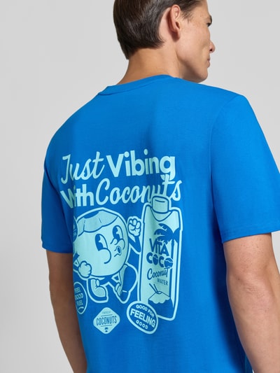 Männermodel trägt Regular Fit T-Shirt aus reiner Baumwolle Modell 'VIBING COCO' von REVIEW in Blau mit großem Print auf der Rückseite, Ganzkörperansicht Rückansicht. Herren T-Shirt von REVIEW x ANSON´S, Rückenlänge Größe M: 68 cm.