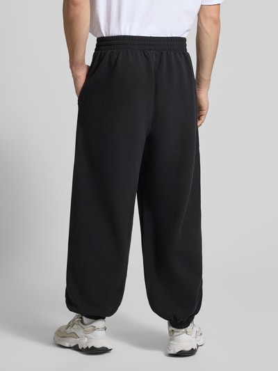 Männermodel trägt Comfort Fit Sweatpants mit Logo-Print von adidas Sportswear in Unifarben mit elastischem Bund und Beinabschluss, Sweat, Ganzkörperansicht Rückansicht.