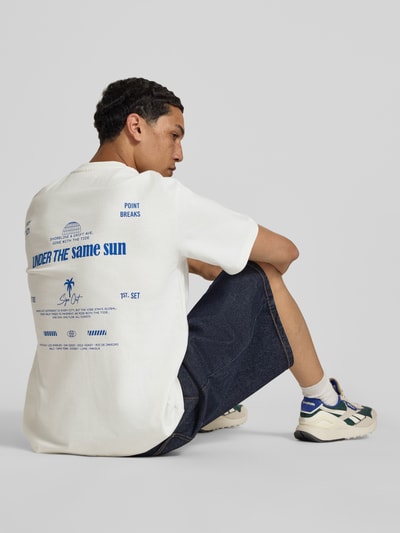 Männermodel trägt Herren T-Shirt mit Statement-Print und Rundhalsausschnitt von Redefined Rebel, Baumwoll-Mix, Relaxed-Fit, Modell 'Bruno', Rückenlänge 70 cm, Größe M, Farbe Weiß mit blauem Print, lockere Passform, strukturierte Oberfläche, Ganzkörperansicht Rückansicht.