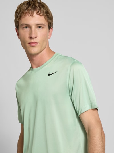 Męski model nosi T-Shirt mit Logo-Print und Rundhalsausschnitt von NIKE TRAINING w kolorze jasnej zieleni, krój regular fit, zbliżenie na górną część ciała