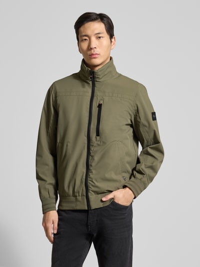 Männermodel trägt Comfort Fit Blouson mit geripptem Rumpfabschluss von Tom Tailor in Oliv, unifarben, Stehkragen, Reißverschluss, Ganzkörperansicht von vorne.