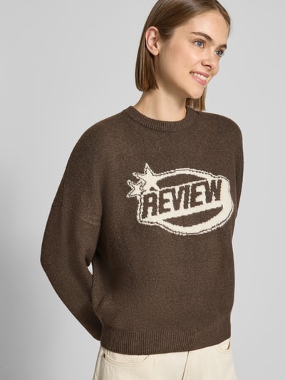 Frauenmodel trägt Strickpullover mit Label-Print von REVIEW in Braun mit Rundhalsausschnitt, geripptem Saum, Nahaufnahme Oberkörper.