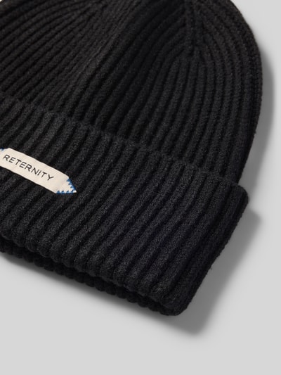 Produktfoto, schwarze Mütze in Strick-Optik Modell 'L’ATELIER' von RETERNITY mit breitem Umschlag und Label-Detail auf hellem Hintergrund