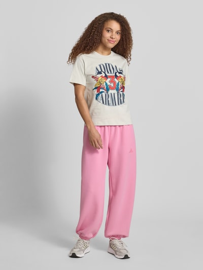 Vrouwenmodel draagt T-shirt met Label-Print van adidas Sportswear in gebroken wit met kleurrijke print, puur katoen, regular fit, ronde hals, ruglengte bij maat S 61 cm, geheel aanzicht van voren.
