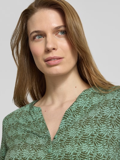 Frauenmodel trägt Regular Fit Schlupfbluse aus reiner Viskose von Christian Berg Woman mit floralem Allover-Print, grün gemustert, Nahaufnahme Oberkörper.