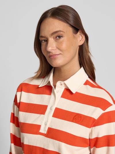 Frauenmodel trägt Longsleeve mit Label-Stitching von Jake*s Casual, Reine Baumwolle, Regular-Fit, Polokragen, kurze Knopfleiste, cremeweiß mit orangefarbenen Blockstreifen, Rückenlänge bei Größe S 23 cm, Nahaufnahme Oberkörper.
