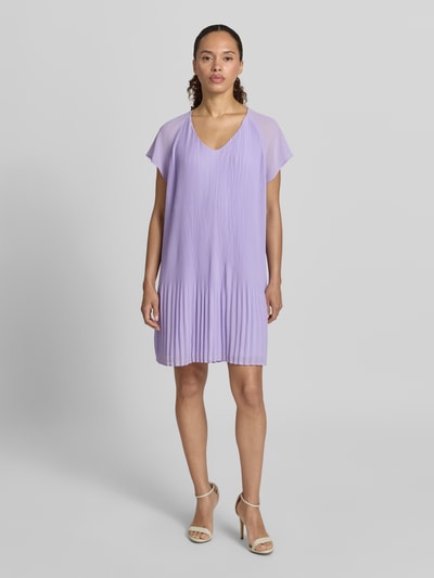 Frauenmodel trägt knielanges Cocktailkleid mit Plisseefalten Modell 'Inken' von GUIDO MARIA KRETSCHMER WOMAN in Flieder, Chiffon, Ganzkörperansicht von vorne.