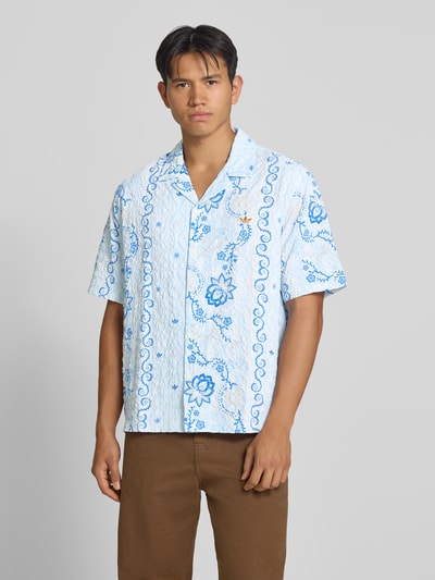 Männermodel trägt Relaxed Fit Freizeithemd aus Seersucker mit Logo-Stitching von adidas Originals, weiß mit blauem Muster, Ganzkörperansicht von vorne. Herren Freizeithemd von adidas Originals.