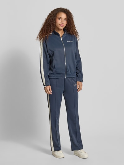 Kobiece modelka nosi spodnie typu track pants z obszyciem koronką model 'TIHANY LACE' od Pegador, mieszanka bawełny, krój regular fit, wyhaftowane logo, kolor granatowy, widok całej sylwetki z przodu.