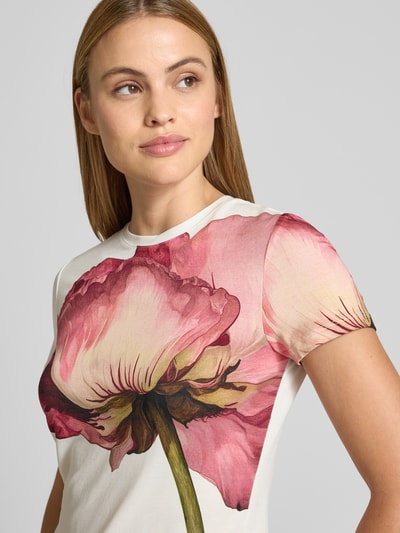 Modelka kobieca nosi T-Shirt z okrągłym dekoltem model 'OBREY' od Ted Baker, biały materiał z dużym różowym kwiatem, viskoza z elastanem, dopasowany krój, damski, zbliżenie na górną część ciała z przodu.