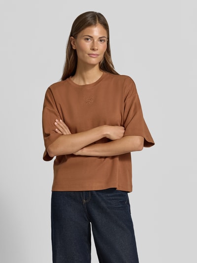 Frauenmodel trägt Oversized T-Shirt aus reiner Baumwolle von s.Oliver RED LABEL in Braun, kombiniert mit dunkler Jeans, Ganzkörperansicht von vorne.