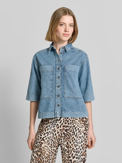 Frauenmodel trägt Relaxed Fit Hemdbluse in Denim-Optik von Emily Van den Bergh aus reiner Baumwolle, Hemdblusenkragen, Halbarm, Brusttaschen, durchgängige Knopfleiste, Ganzkörperansicht von vorne.