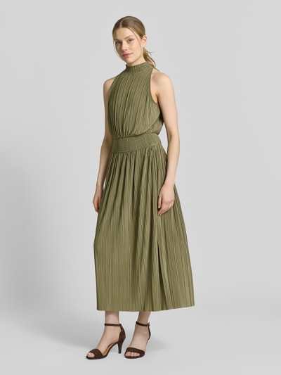 Frauenmodel trägt Plisseekleid mit Smok-Details Modell 'UMA' von Samsøe Samsøe in Olive, taillierter Schnitt, Stehkragen, Midikleid, Ganzkörperansicht von vorne.