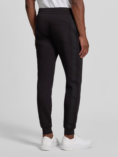 Männermodel trägt schwarze Sweatpants mit Bordüre von Armani Exchange aus elastischem Baumwoll-Mix, seitliche Eingrifftaschen, Ganzkörperansicht Rückansicht.