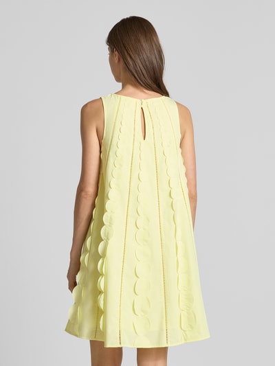 Frauenmodel trägt Minikleid mit rückseitigem Schlüsselloch-Ausschnitt von YAS, gelber Material-Mix mit Baumwoll-Anteil, ausgestellter Schnitt, Modell 'EMMA', feine Kreis-Struktur, Rückseite mit Knopfdetail, Rückenlänge 89 cm, Brustweite 46 cm, Ganzkörperansicht Rückansicht.