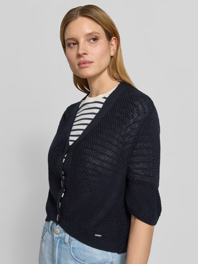 Vrouwenmodel draagt Cardigan mit V-Ausschnitt und 3/4-Arm van More & More in donkerblauw met knoopsluiting, relaxed fit, frontale close-up van bovenlichaam, ruglengte maat 36: 48 cm, mouwlengte maat 36: 24 cm.