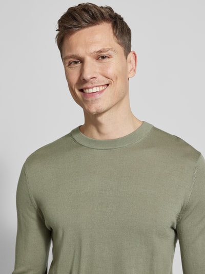 Mężczyzna nosi sweter wełniany Regular Fit Pullover aus reiner Wolle Modell 'TRAY' od SELECTED HOMME, efekt: jednolity kolor, okrągły dekolt, drobny splot, długi rękaw, zakończenia prążkowane, wykończenie materiału: drobny splot, materiał: czysta wełna. Zbliżenie na górną część ciała.