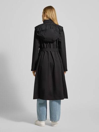 Frauenmodel trägt Regular Fit Mantel mit Stehkragen Modell 'Suva' von Rains in Schwarz mit Pattentaschen, Stoffband, Ganzkörperansicht Rückansicht. Rückenlänge 113 cm, Schulterbreite 42 cm, Brustweite 51 cm, Ärmellänge 62 cm, taillierte Passform.