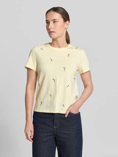 Frauenmodel trägt Damen T-Shirt von Mango aus Reine Baumwolle, Regular-Fit, Modell 'Flowi' mit florales Allover-Stitching, Kurzärmelig, Rundhalsausschnitt, Rückenlänge 55 cm bei Größe S, sanft gelbe Farbe, schlichte Textur, kleine gestickte Blumen, Ganzkörperansicht von vorne.