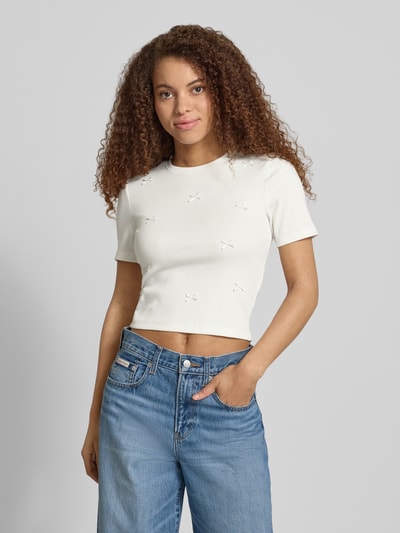 Frauenmodel trägt Slim Fit T-Shirt aus Baumwoll-Mix Modell 'FEMKE' von Only, unifarben, Kurzarm, Schleifen, Feinripp, Ganzkörperansicht von vorne.
