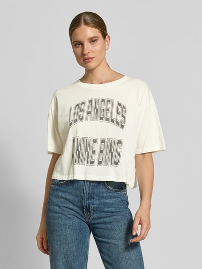 Vrouwenmodel draagt Cropped T-Shirt met Labelprint van Anine Bing in offwhite, puur katoen, kort, losse pasvorm, ruglengte maat S 42 cm, voorkant bovenlichaam close-up.