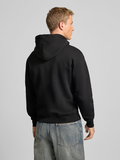 Männermodel draagt Hoodie met Labelstitching Model 'Camo Sleeve' van Alpha Industries, katoenmix, regular fit, ruglengte M 67 cm, mouwlengte 66 cm, kangoeroezak, zwarte kleur, gladde textuur, ganzkörperansicht rückansicht.