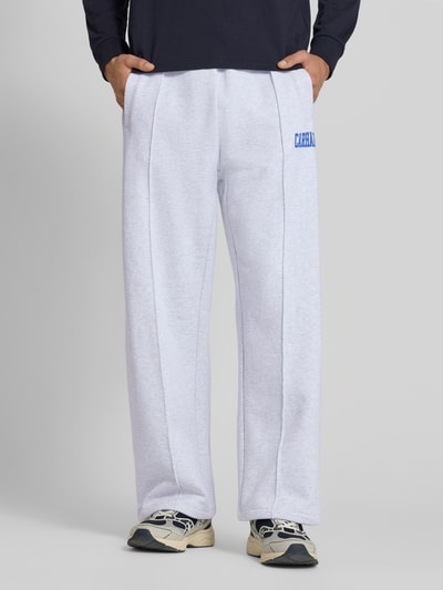 Männermodel trägt Sweatpants mit elastischem Bund und Label-Print von Carhartt Work In Progress aus Reine Baumwolle in Hellgrau mit blauen Label-Print, sichtbare Längsnähte, Wide Leg, Modell 'Pond Corps', Ganzkörperansicht von vorne.