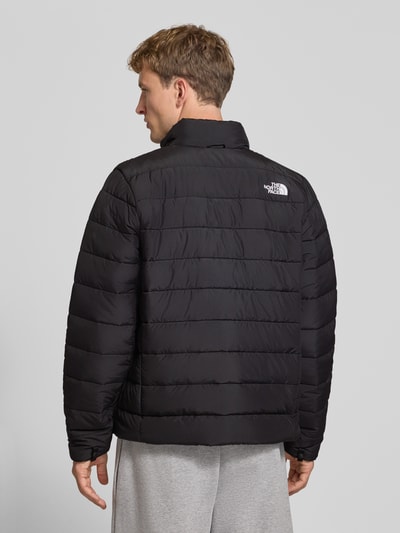 Männermodel trägt Regular Fit Jacke in Stepp-Optik Modell 'ACONCAGUA' von The North Face, schwarze Farbe, Ganzkörperansicht Rückansicht. Rückenlänge 70 cm, Schulterbreite 46 cm, Brustweite 58 cm, Ärmellänge 70 cm, Stehkragen, Logo-Stitching, Reißverschluss, klassische gestreifte Steppung.
