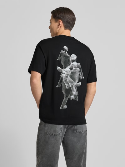 Männermodel trägt Regular Fit T-Shirt aus reiner Baumwolle Modell 'DOLLO' von HUGO in Schwarz mit grafischem Muster und Label Stitching, Ganzkörperansicht Rückansicht.
