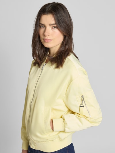 Kobiece modelka nosi Regular Fit Bomberjacke mit College-Kragen od s.Oliver RED LABEL, efekt: jednolity kolor, satyna, długi rękaw, wpuszczane kieszenie, brustasza, zawieszka z logo, zamek błyskawiczny, prążkowane zakończenie rękawów i dołu, jasny odcień, gładka faktura, widok całej sylwetki z przodu.