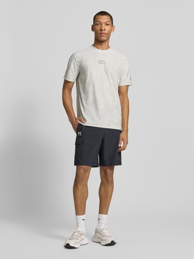 Männermodel trägt T-Shirt mit Rundhalsausschnitt und Label-Detail von EA7 Emporio Armani, regular fit, lichte tinten, Ganzkörperansicht von vorne