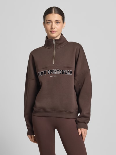 Frauenmodel trägt Sweatshirt mit Stehkragen und Reißverschluss von aim'n in Dunkelbraun, Baumwoll-Mix, Relaxed Fit, Label-Print, Ganzkörperansicht von vorne.
