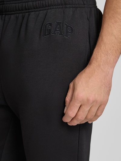 Männermodel trägt Sweatpants mit Logo und elastischem Bund von GAP in Schwarz aus Baumwoll-Mix, Regular-Fit, Nahaufnahme Oberschenkel.