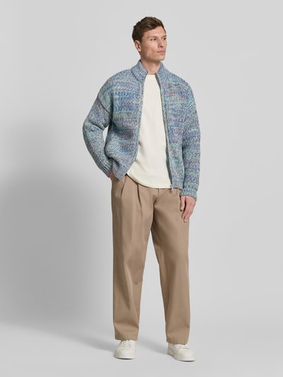 Männermodel trägt Relaxed Fit Strickjacke aus Baumwoll-Woll-Mix mit Viskose-Anteil Modell 'UN-WASTED' von Armedangels, mehrfarbig, Strickoptik, Reißverschluss, Logo-Detail, Stehkragen, langarm, gerippte Abschlüsse, seitliche Eingrifftaschen, Ganzkörperansicht von vorne.