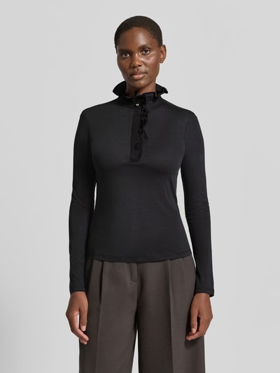 Modelka prezentuje bluzkę z długim rękawem Longsleeve mit Rüschen od Rich & Royal, mieszanka lyocellu i bawełny, taliowany krój, kołnierz z ukrytą listwą guzikową i falbanami, długość tyłu w rozmiarze 36: 60 cm, widok całej sylwetki z przodu.
